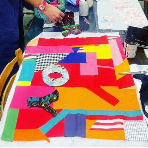 Image of quilting workstation, brightly coloured material and two people working 