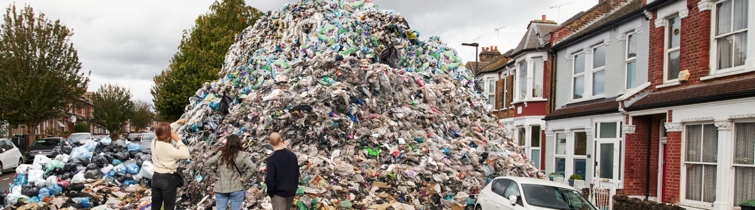 Three people look at a mountain of waste in the middle of a local street