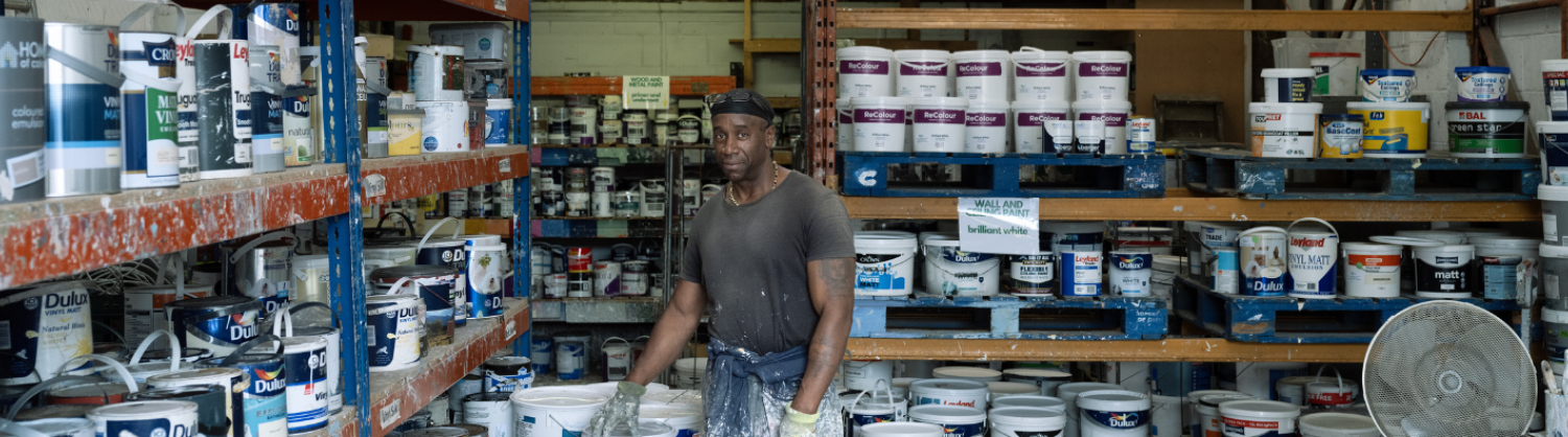 A man stands in a warehouse full of paint tins