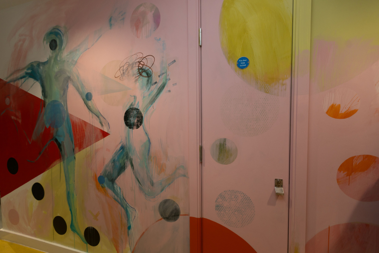 Laura McKendry's pink wall mural with two blue figures moving in front of colourful circles