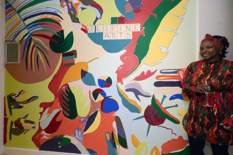 Leanne Ingram standing next to her wall mural of colourful objects including leaves and feathers