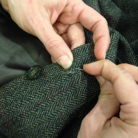 Hands sewing a coat button back on